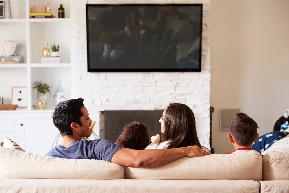Back view of family of four sitting on the sofa watching television