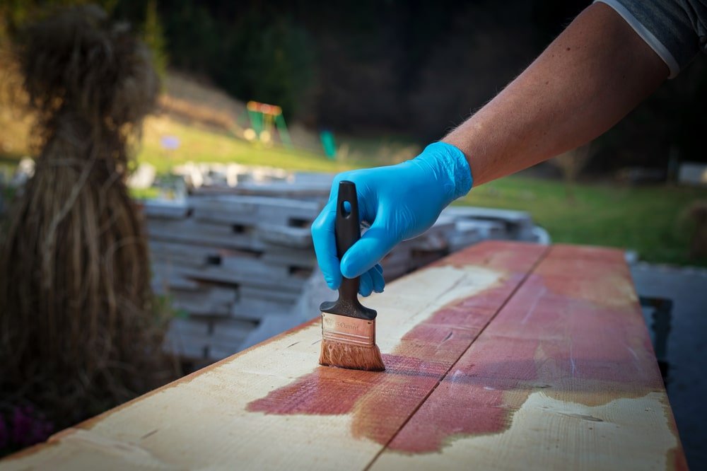 Gloved hand applying wood stain on wooden surface