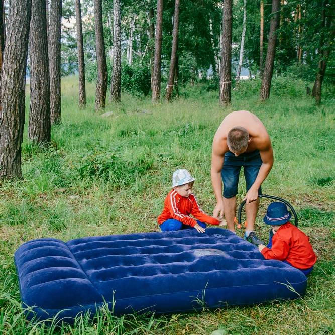 a man with children pumped up blue air mattress in forest