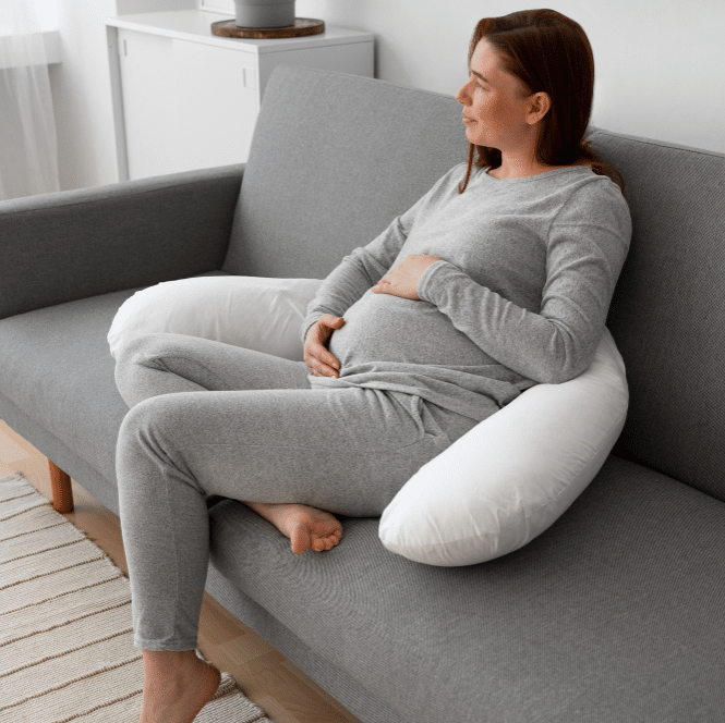 a pregnant woman sitting on a couch using a pregnancy pillow