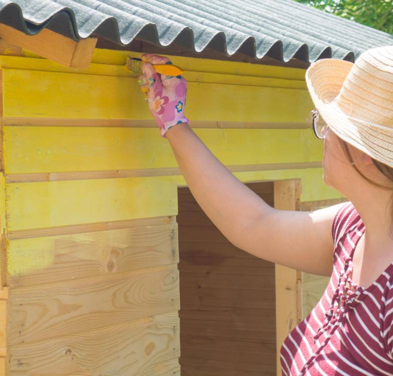 a woman painting a garden shed yellow paint