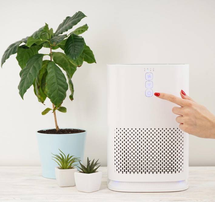 a woman turning on a modern air purifier