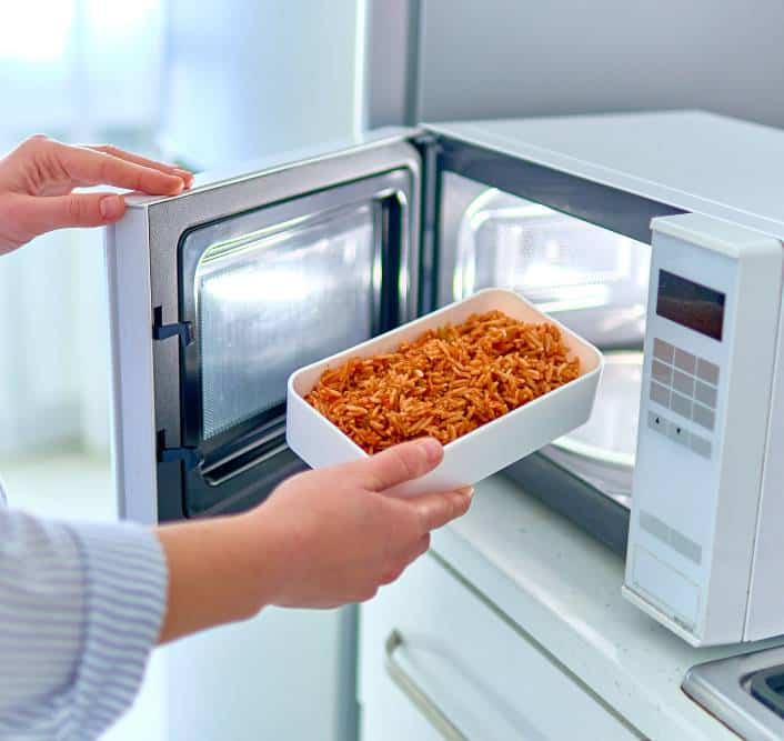 a woman warming up a container of food in a microwave