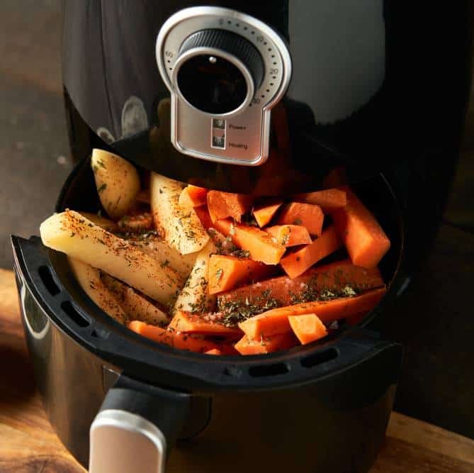 cooking potatoes and carrot sticks with spices in an air fryer