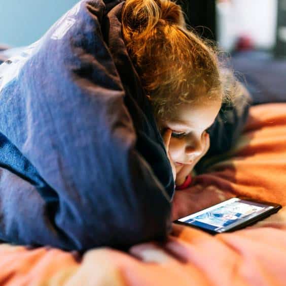 girl using smartphone under blanket