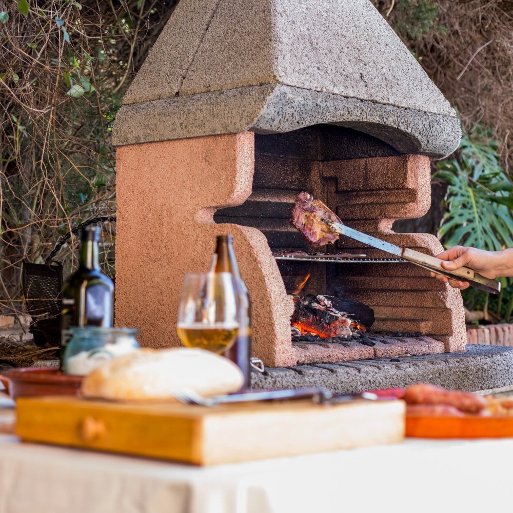 holding grilled meat with tong in outdoor barbecue